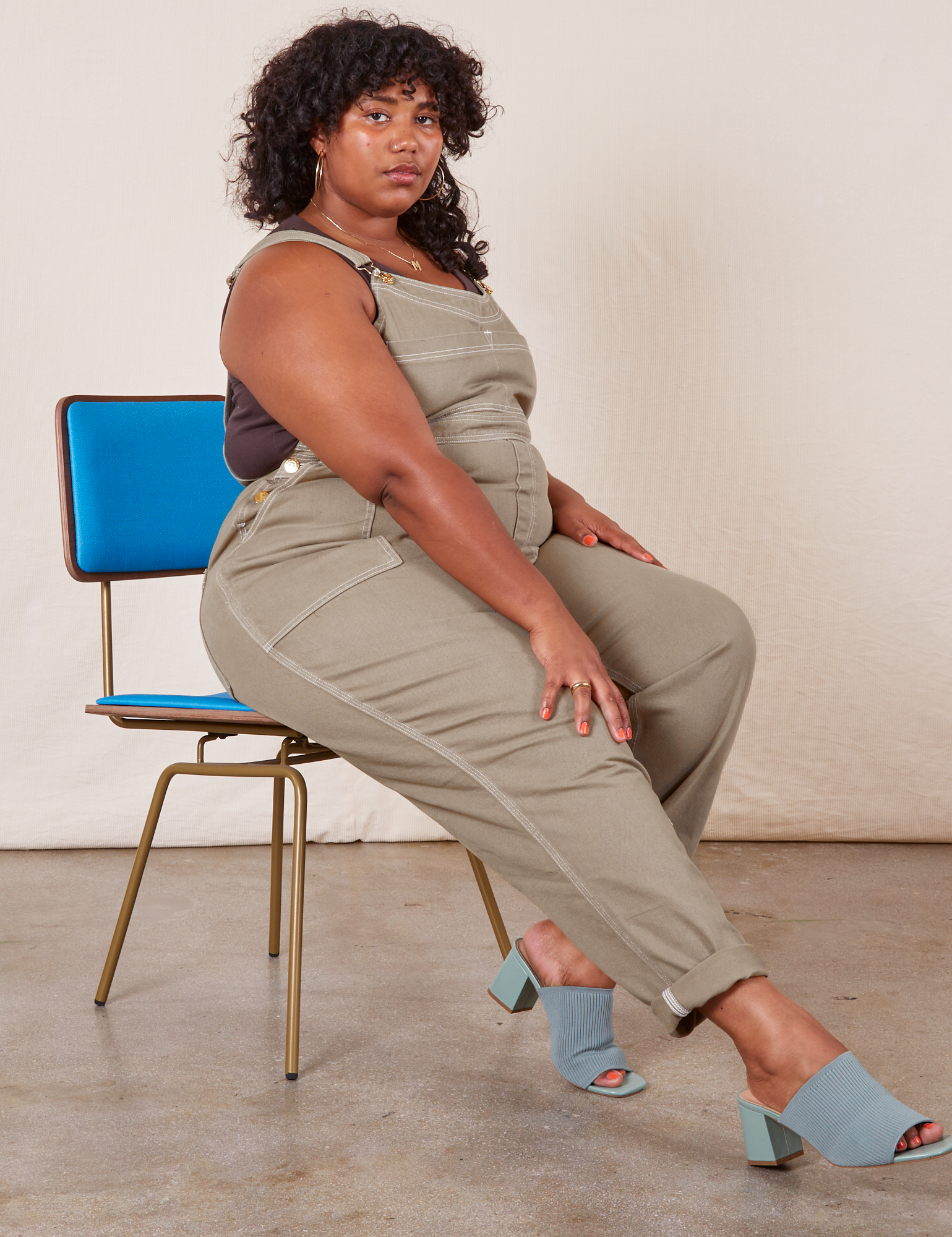 Side view of Original Overalls in Khaki Grey worn by Morgan sitting in a blue chair