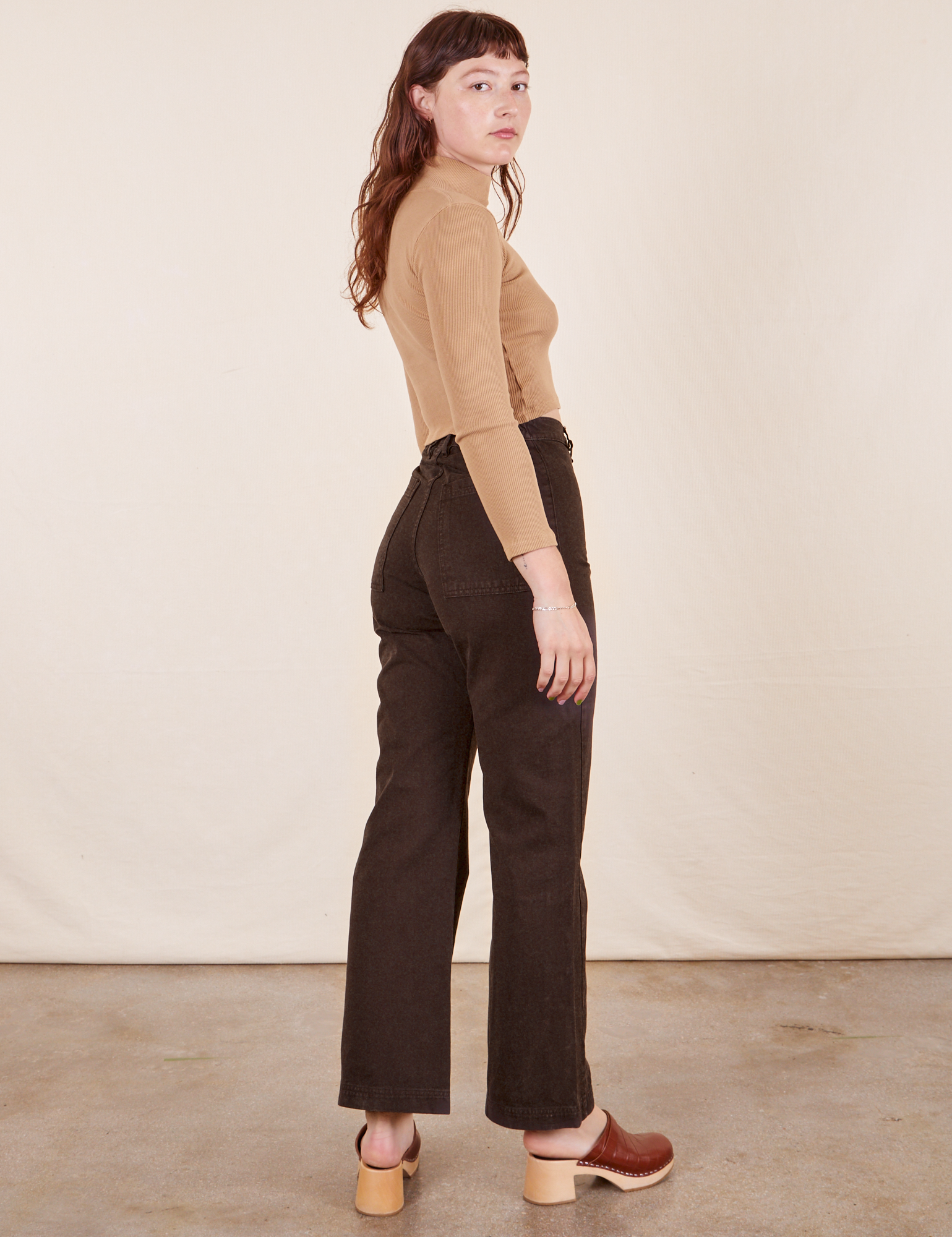 Side view of Western Pants in Espresso Brown paired with tan Essential Turtleneck worn by Alex.