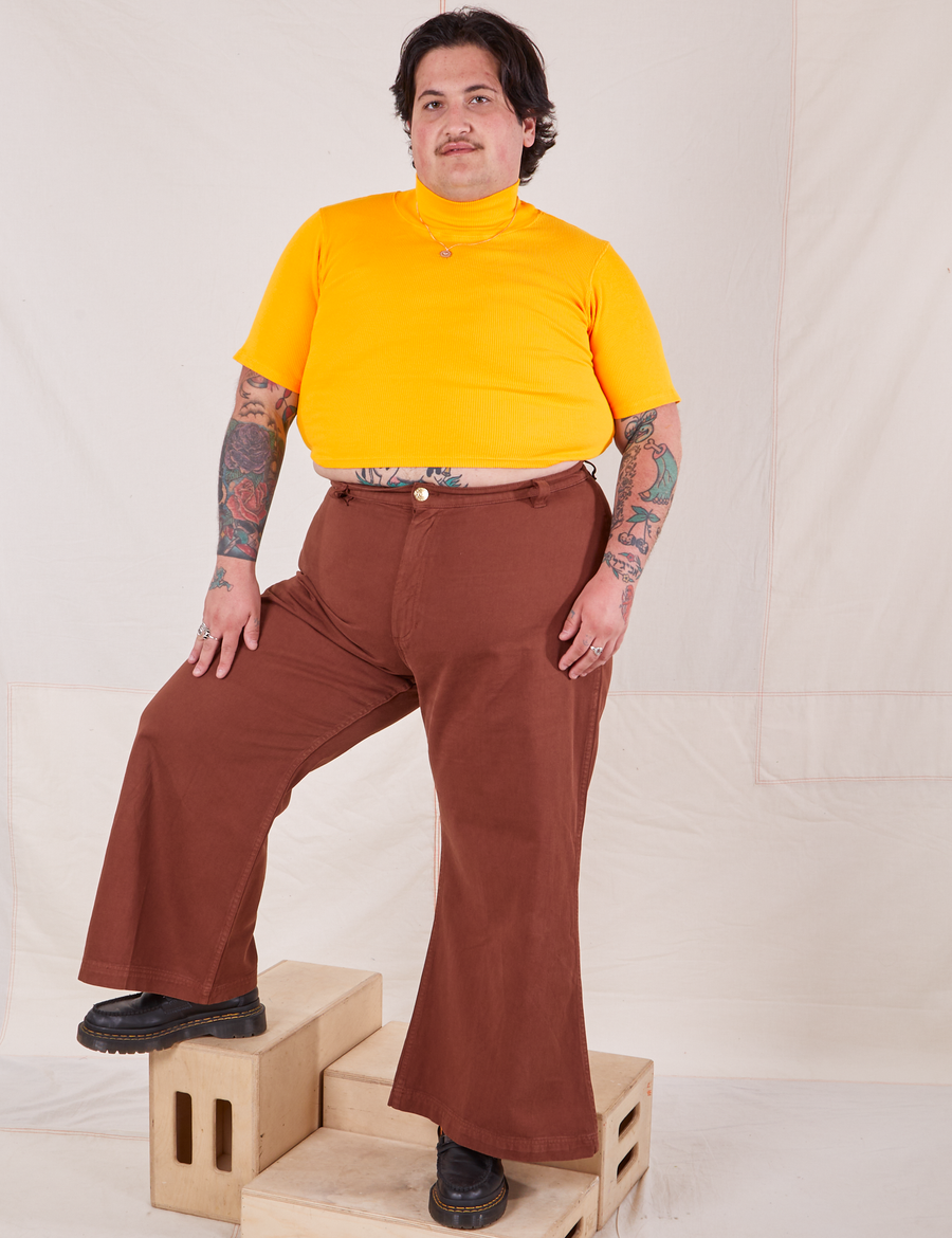 Sam is wearing XL 1/2 Sleeve Essential Turtleneck in Sunshine Yellow paired with fudgesicle brown Bell Bottoms