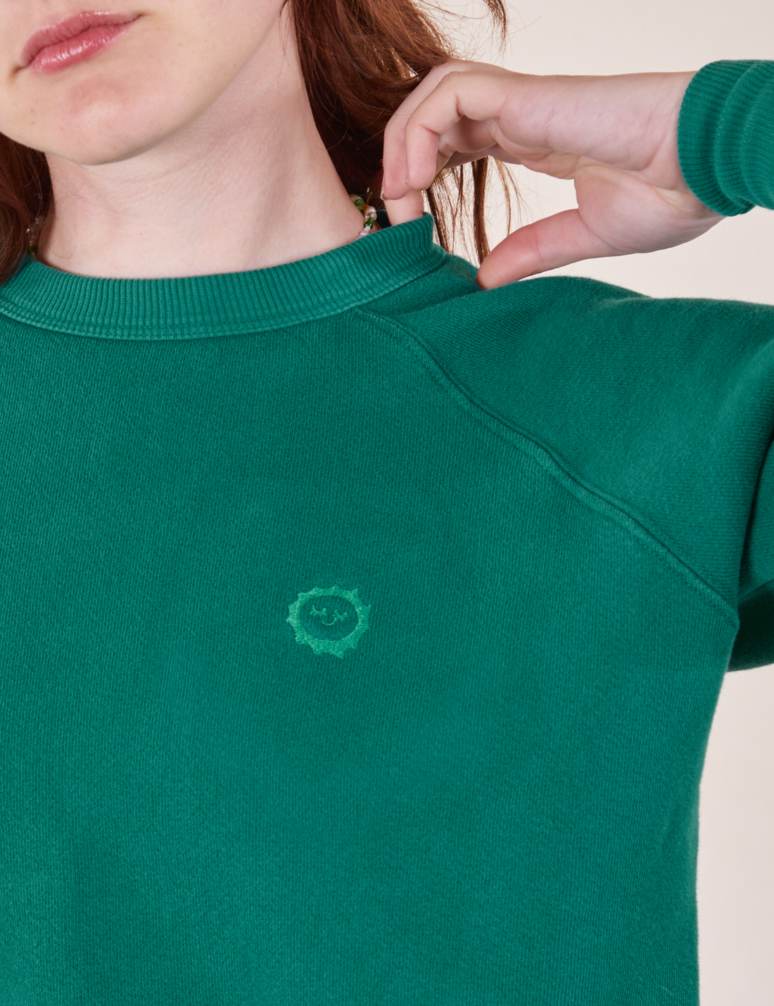 Heavyweight Crew in Hunter Green front close up on Alex. Embroidered sun baby logo in green