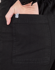 Back pocket close up of Everyday Jumpsuit in Basic Black. Alex has her hand in the pocket. 