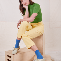 Alex is wearing 1/2 Sleeve Essential Turtleneck in Bright Olive. She is sitting on a wooden crate.