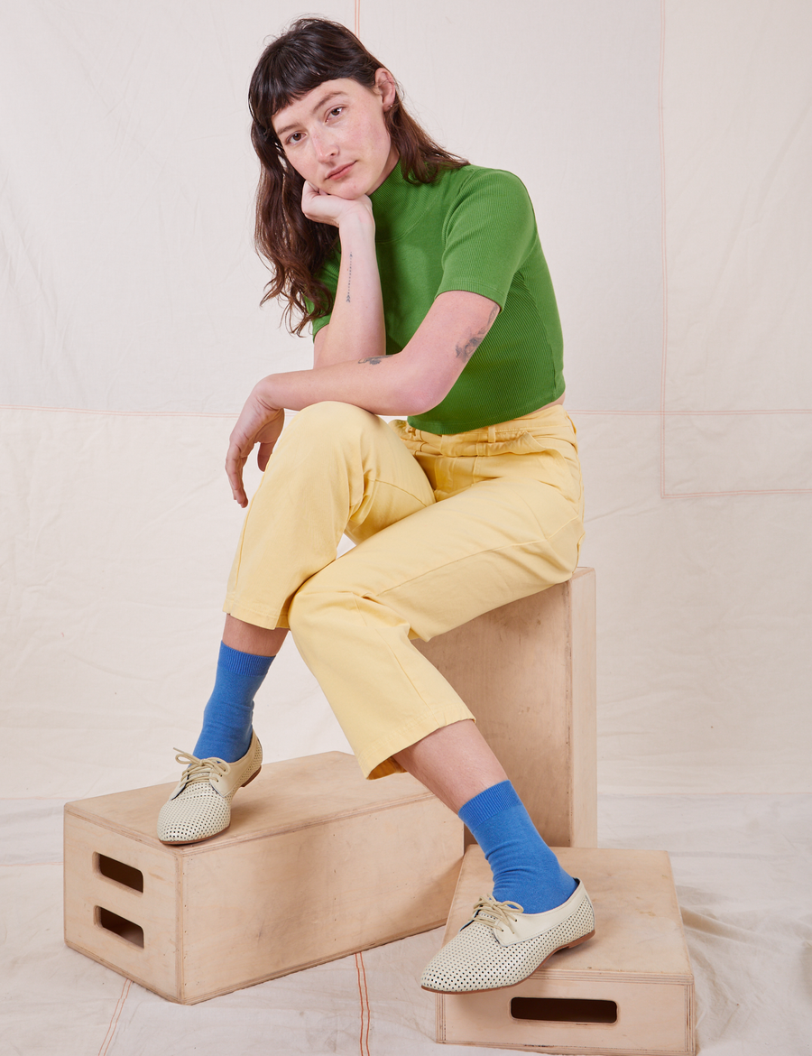 Alex is wearing 1/2 Sleeve Essential Turtleneck in Bright Olive. She is sitting on a wooden crate.