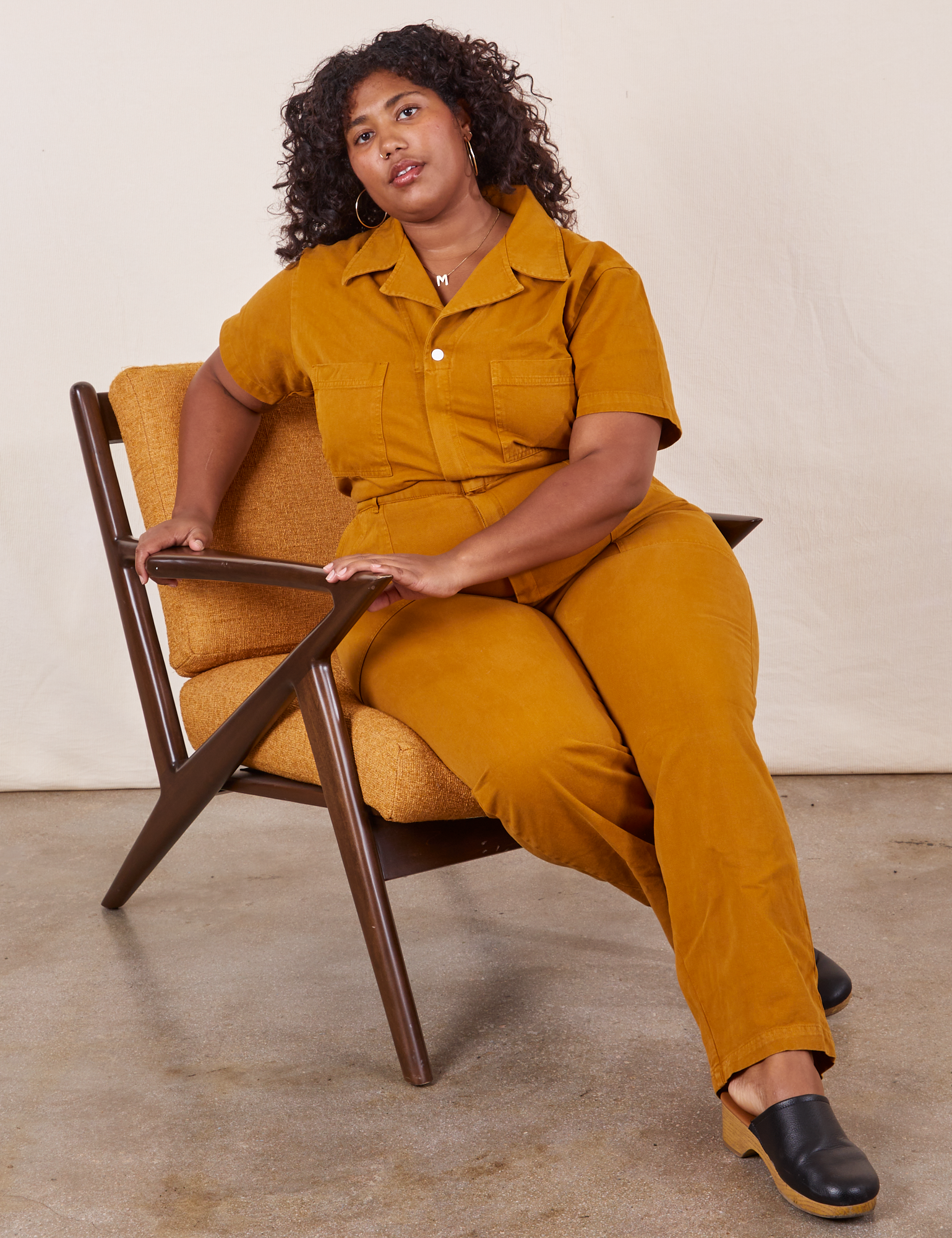 Morgan is sitting in a chair wearing Short Sleeve Jumpsuit in Spicy Mustard
