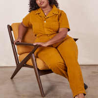 Morgan is sitting in a chair wearing Short Sleeve Jumpsuit in Spicy Mustard