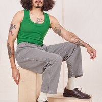 Jesse is sitting on a wooden crate wearing Checker Trousers in Black & White and forest green Tank Top
