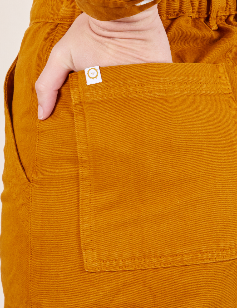Back pocket close up of Everyday Jumpsuit in Spicy Mustard. Alex has her hand in the pocket.