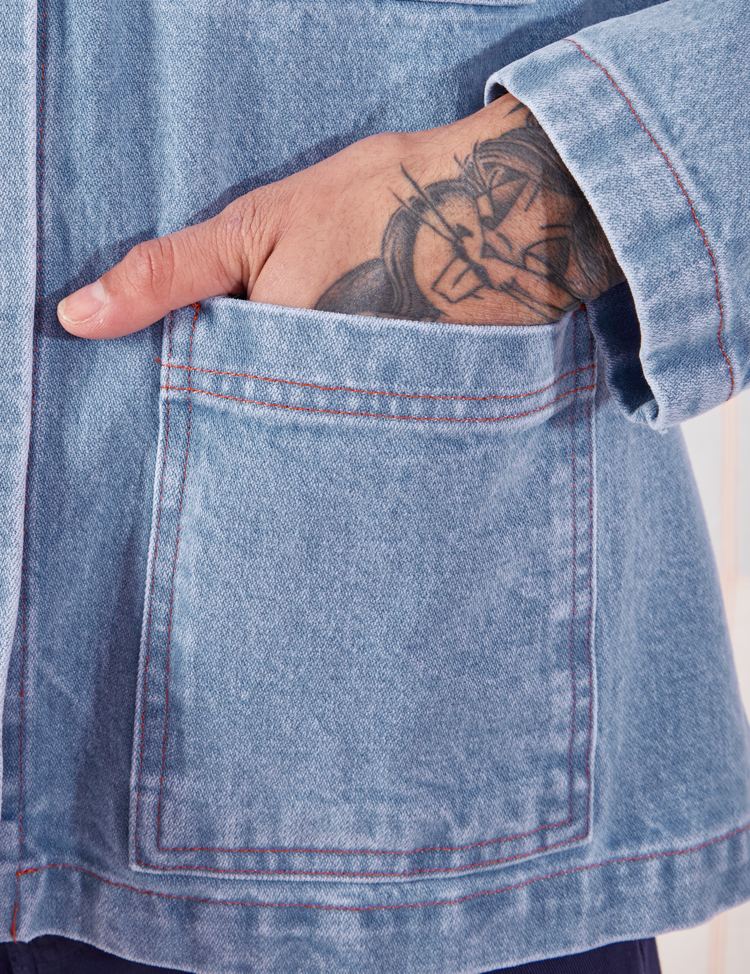 Front pocket close up of Indigo Denim Work Jacket in Light Wash. Jesse has their hand in the pocket.