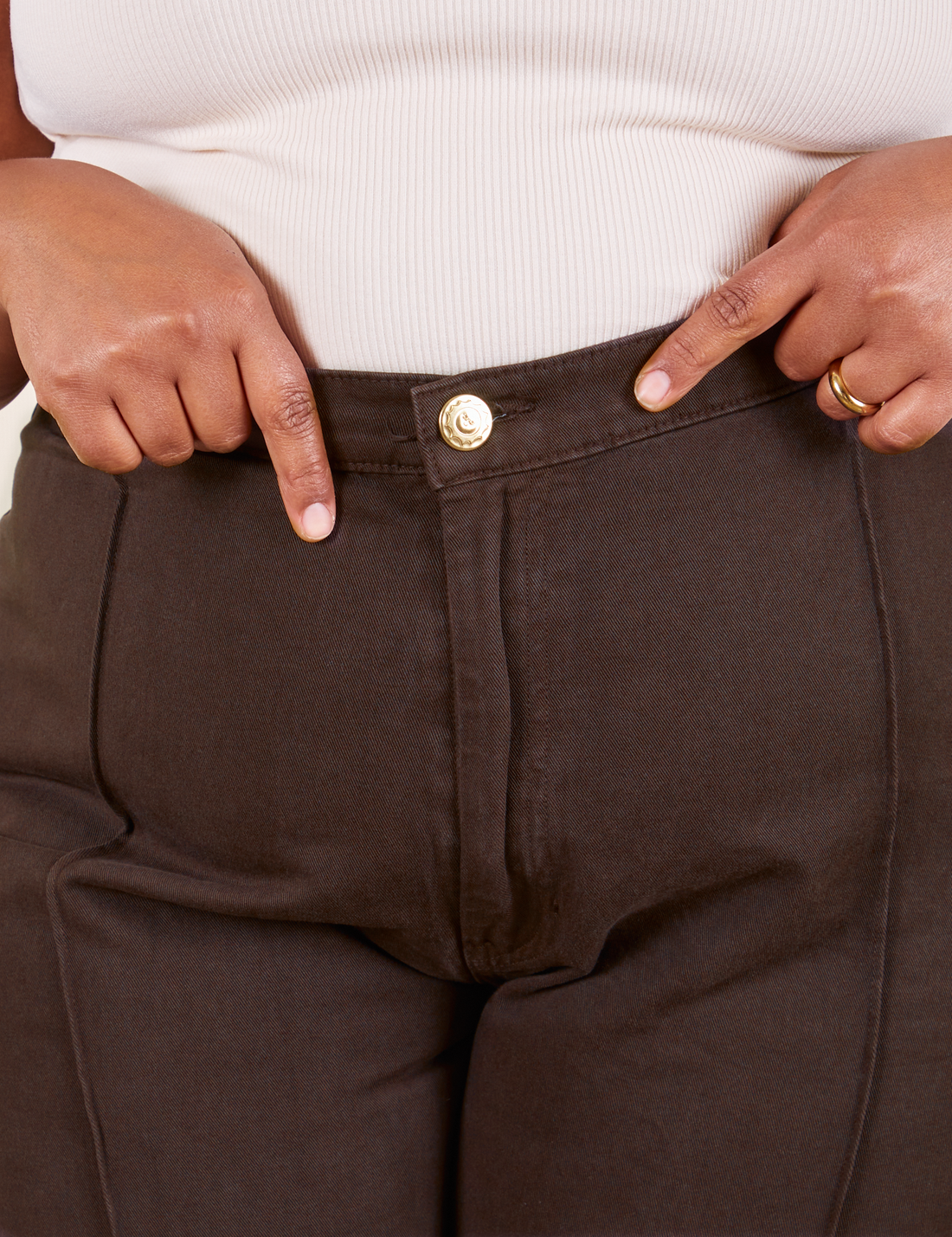 Front close up of Western Pants in Espresso Brown. Worn by Morgan holding the waistband edge of the pants.