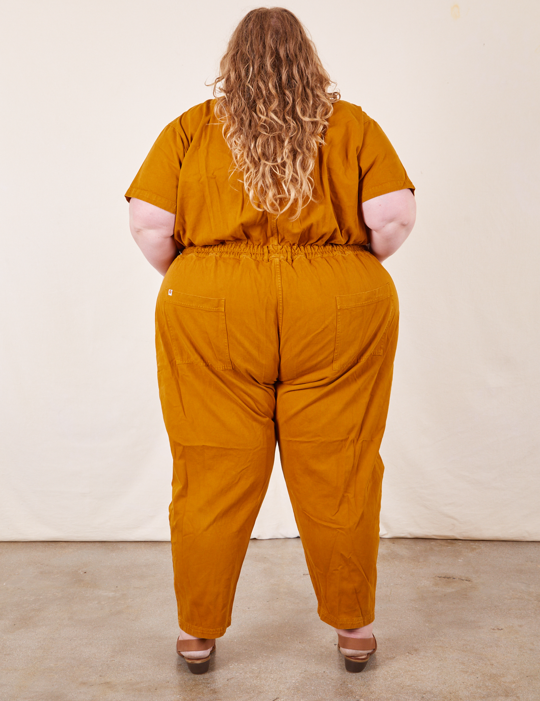 Back view of Short Sleeve Jumpsuit in Spicy Mustard worn by Catie
