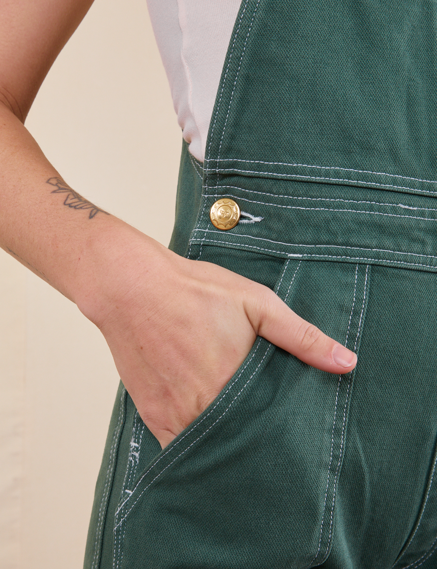 Front pocket close up of Original Overalls in Dark Emerald Green. Alex has her hand in the pocket.