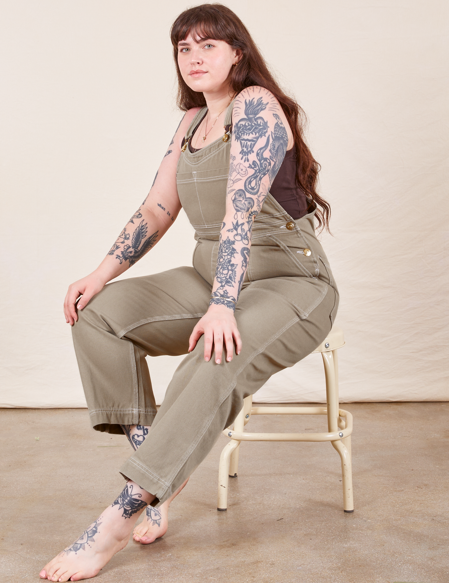 Sydney is sitting on a stool wearing Original Overalls in Khaki Grey