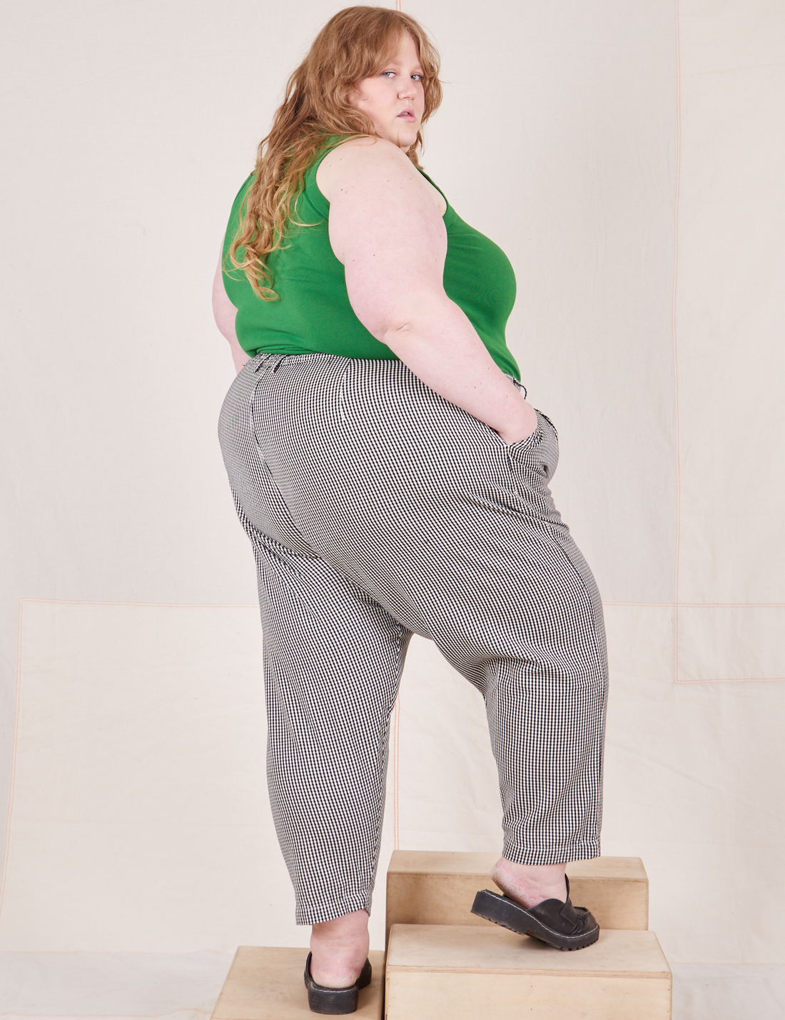 Angled back view of Checker Trousers in Black & White and forest green Tank Top worn by Catie