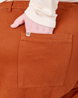 Back pocket close up of Organic Work Pants in Burnt Terracotta. Catie has her hand in the pocket.