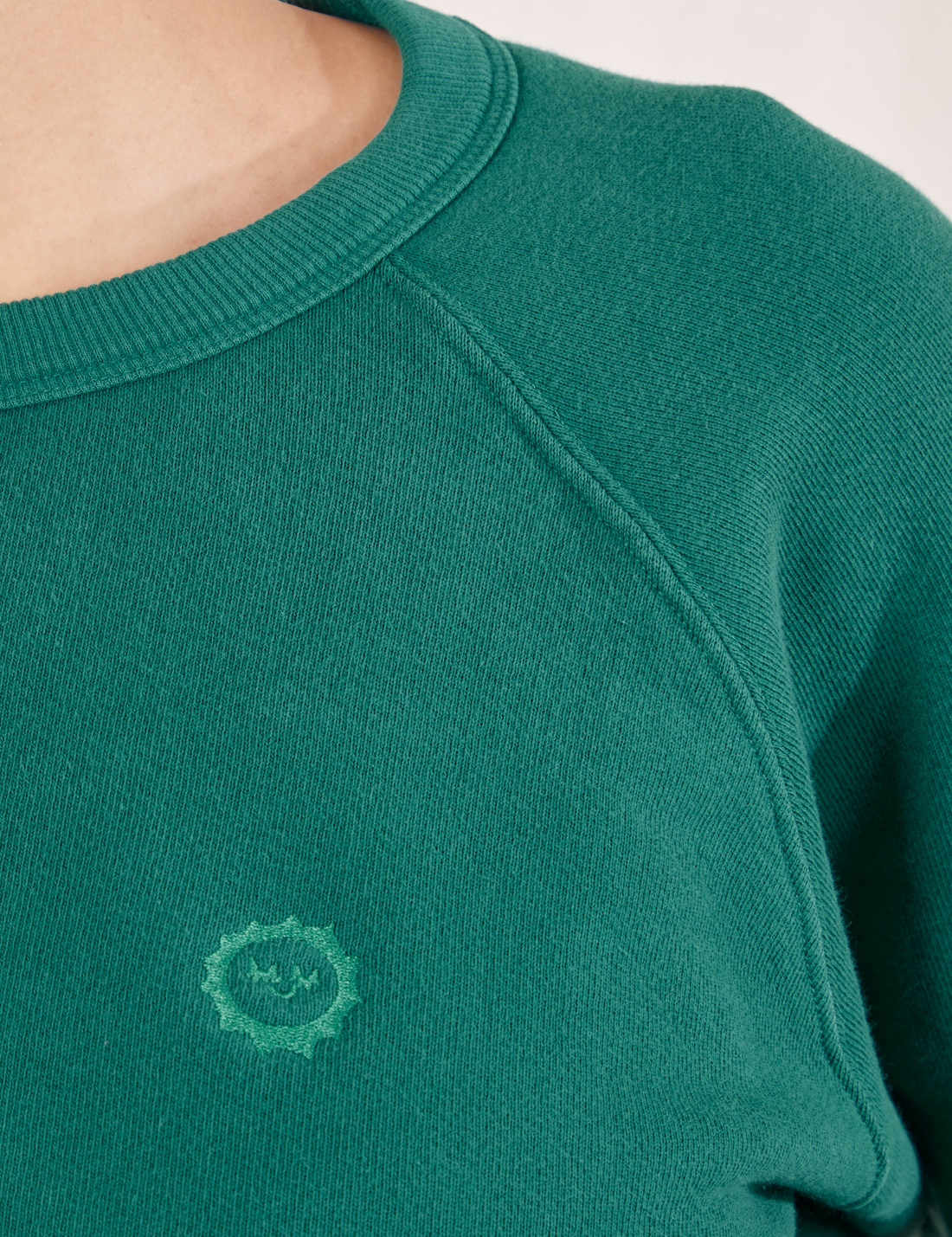 Heavyweight Crew in Hunter Green front close up on Tiara. Embroidered sun baby logo in green.
