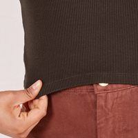 Bottom close up of 1/2 Sleeve Essential Turtleneck in Espresso Brown. Mika is holding the edge of the hem.