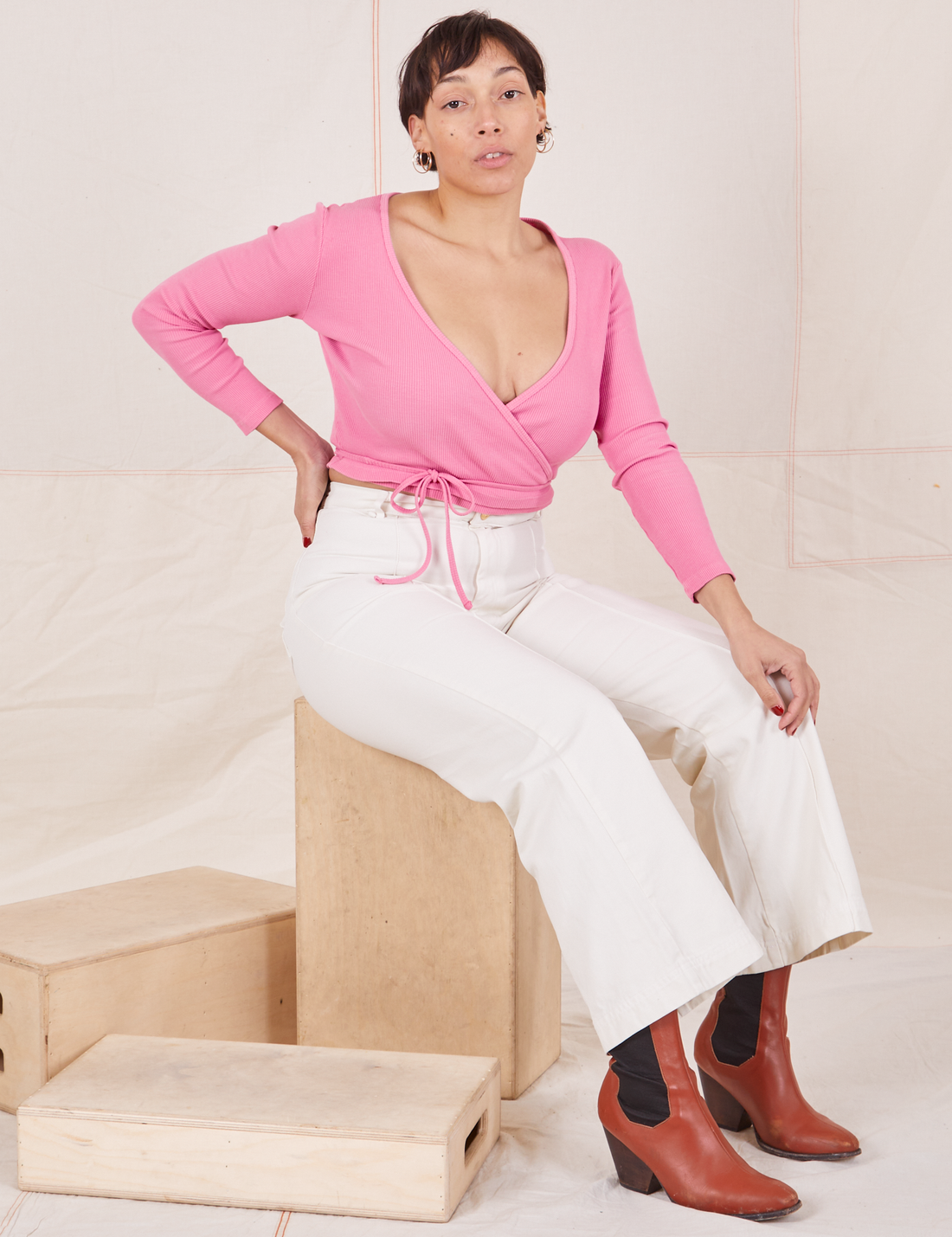 Wrap Top in Bubblegum Pink on Tiara wearing vintage off-white Western Pants sitting on wooden crate