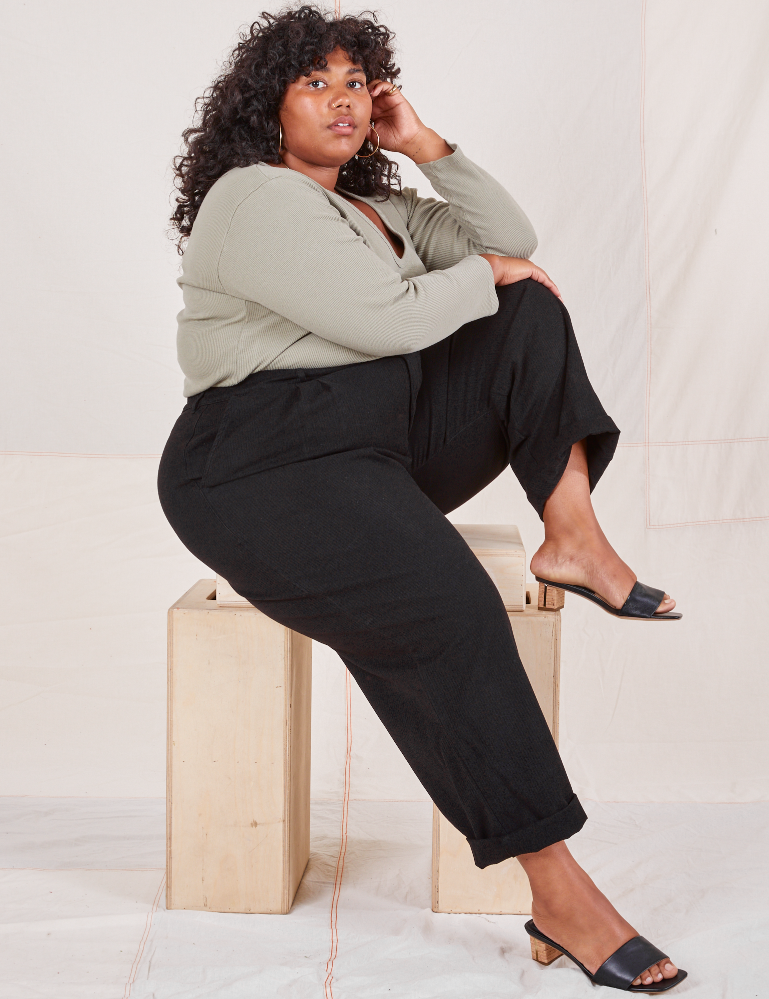 Heritage Trousers in Basic Black side view on Morgan sitting on wooden crate wearing khaki grey Long Sleeve V-Neck Tee