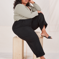 Heritage Trousers in Basic Black side view on Morgan sitting on wooden crate wearing khaki grey Long Sleeve V-Neck Tee