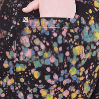 Marble Paint Splatter Work Pants back pocket close up on Catie with hand in pocket. Sun baby logo tag on pocket