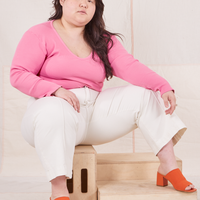Ashley is sitting on a wooden crate wearing Long Sleeve V-Neck Tee in Bubblegum Pink and vintage off-white Western Pants