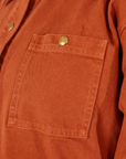 Denim Work Jacket in Burnt Terracotta front pocket close up with sun baby brass button