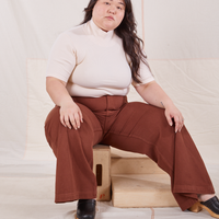 Ashley is sitting on a wooden crate wearing 1/2 Sleeve Essential Turtleneck in Vintage Off White and fudgesicle brown Bell Bottoms