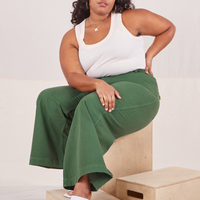 Morgan is sitting on a wooden crate wearing Bell Bottoms in Dark Emerald Green and vintage off-white Tank Top