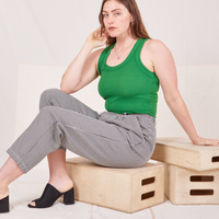 Allison is sitting on a wooden crate. She is wearing Checker Trousers in Black & White and forest green Tank Top