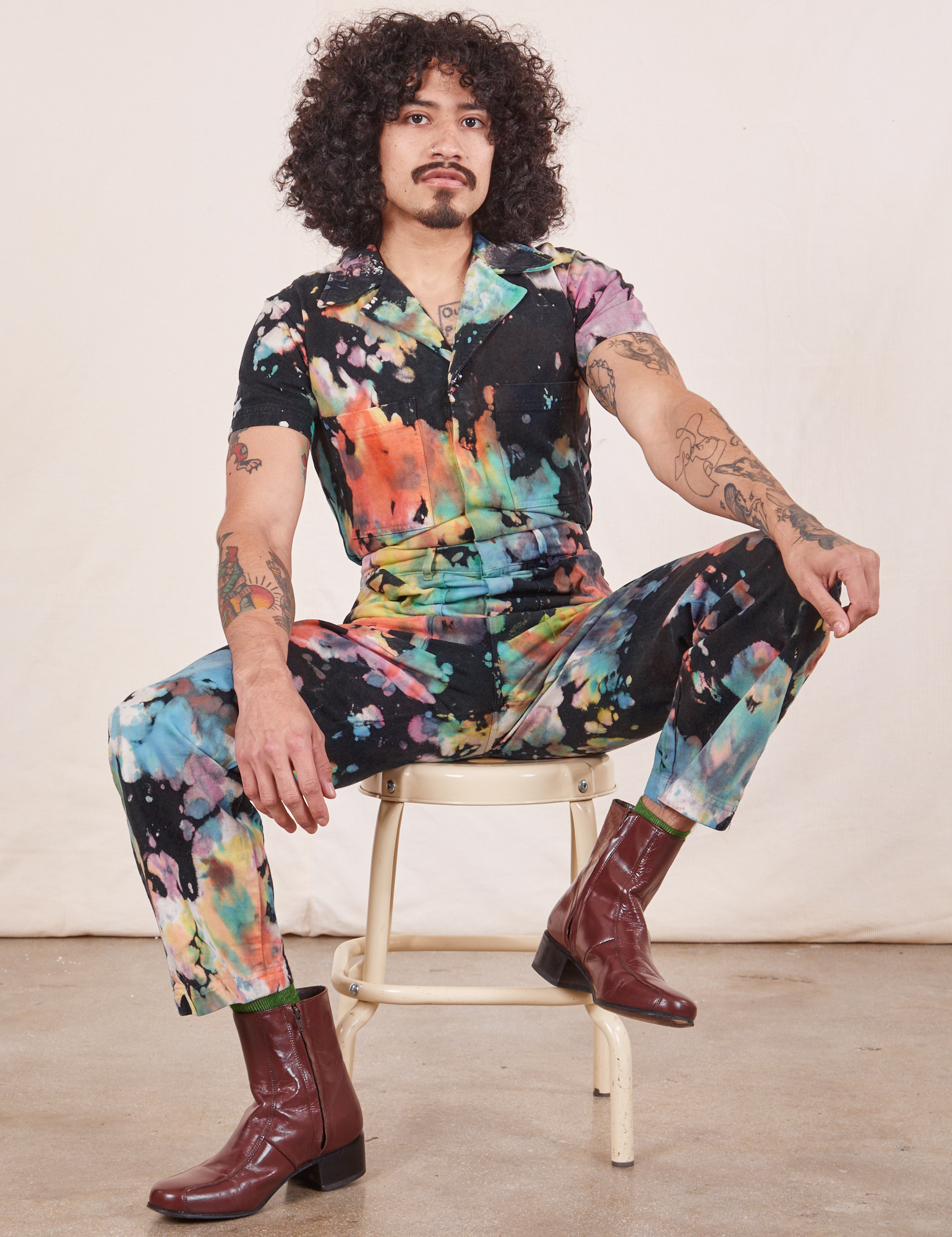 Short Sleeve Jumpsuit in Rainbow Magic Waters on Jesse sitting on vintage stool