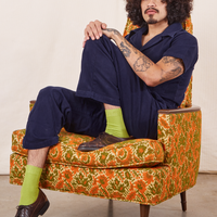 Jesse is sitting in an upholstered chair wearing Short Sleeve Jumpsuit in Navy Blue