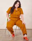 Ashley is sitting on a chair wearing Short Sleeve Jumpsuit in Spicy Mustard