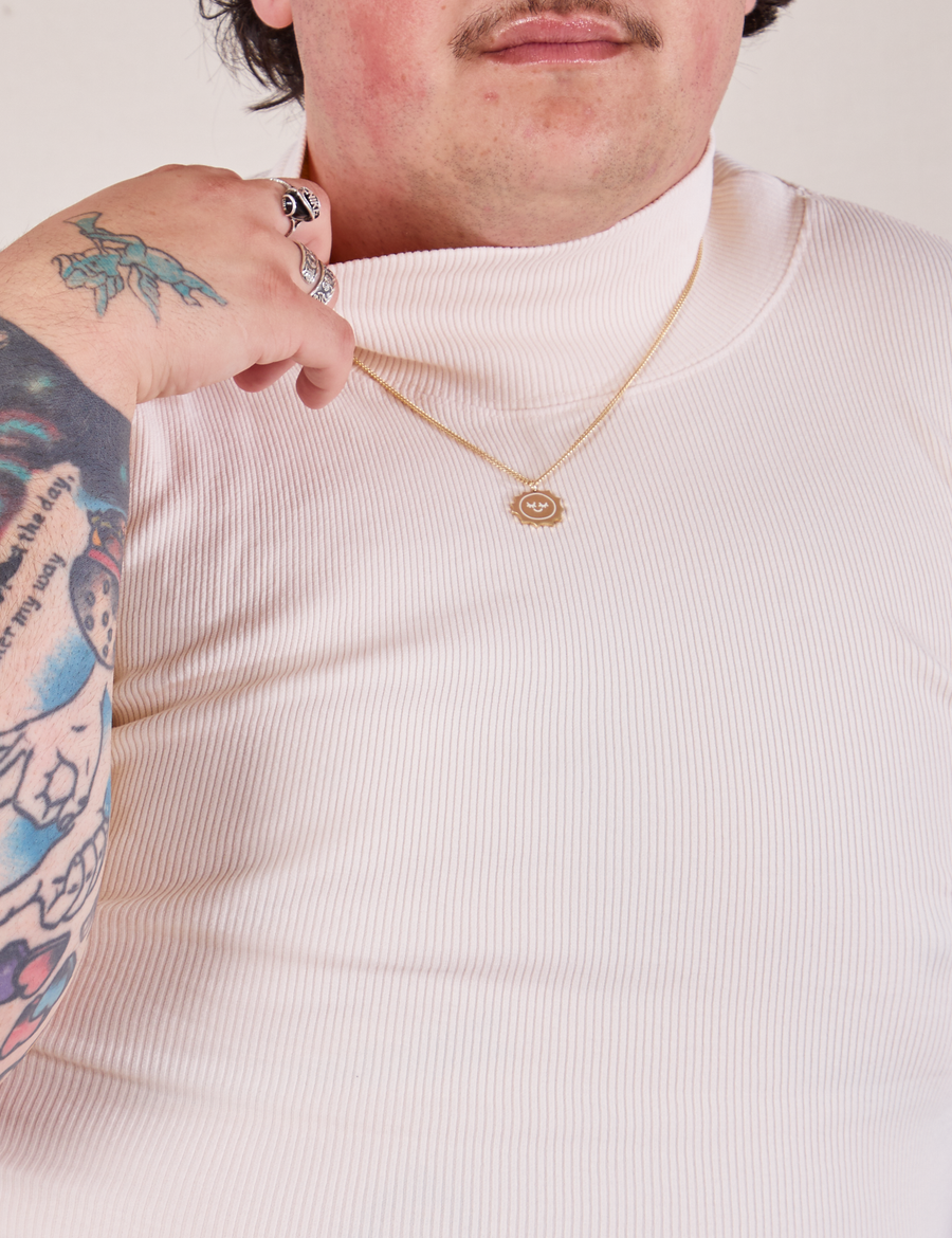 Front close up of 1/2 Sleeve Essential Turtleneck in Vintage Off White. Sam is holding the edge of the turtleneck