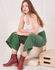 Allison is sitting on a wooden crate wearing Bell Bottoms in Dark Emerald Green and vintage off-white Tank Top