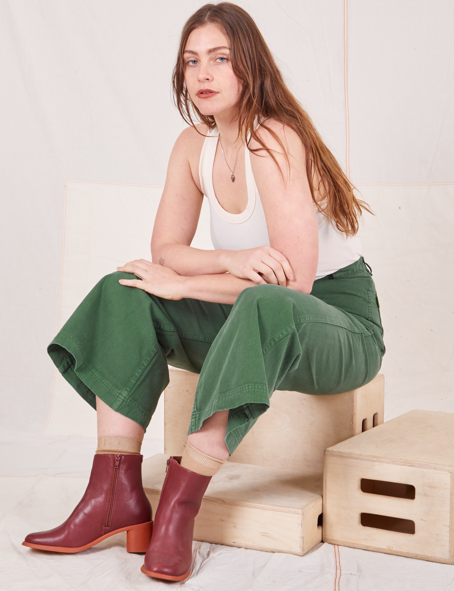 Allison is sitting on a wooden crate wearing Bell Bottoms in Dark Emerald Green and vintage off-white Tank Top