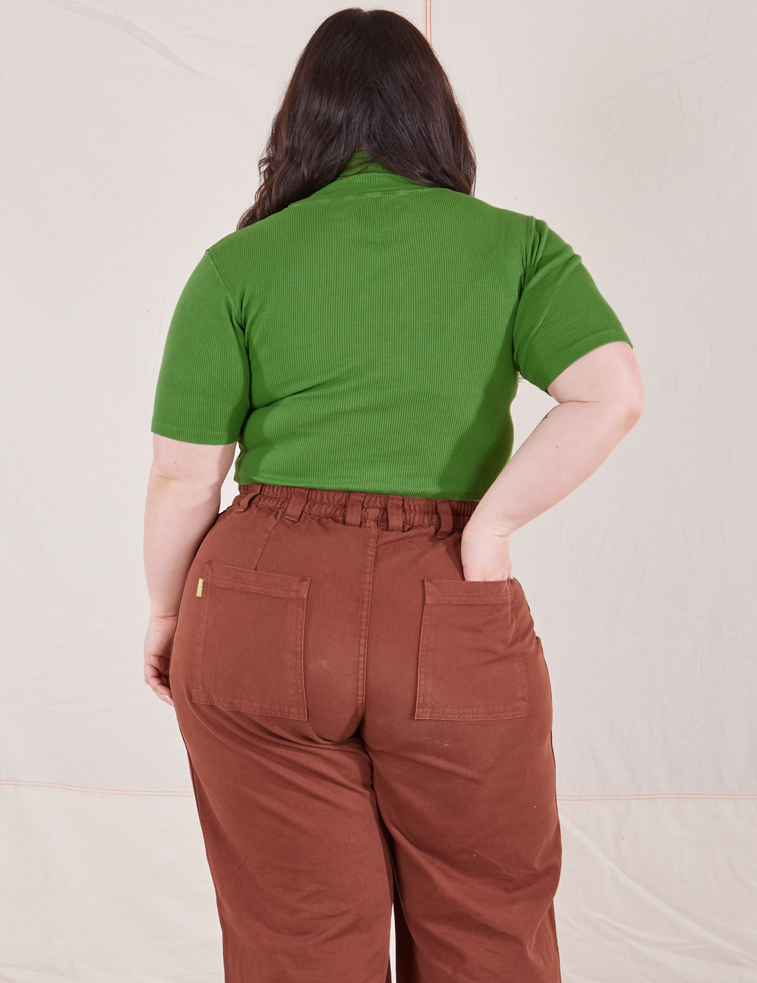 1/2 Sleeve Essential Turtleneck in Bright Olive back view on Ashley wearing fudgesicle brown Bell Bottoms. Ashley has her hand in the back pocket.