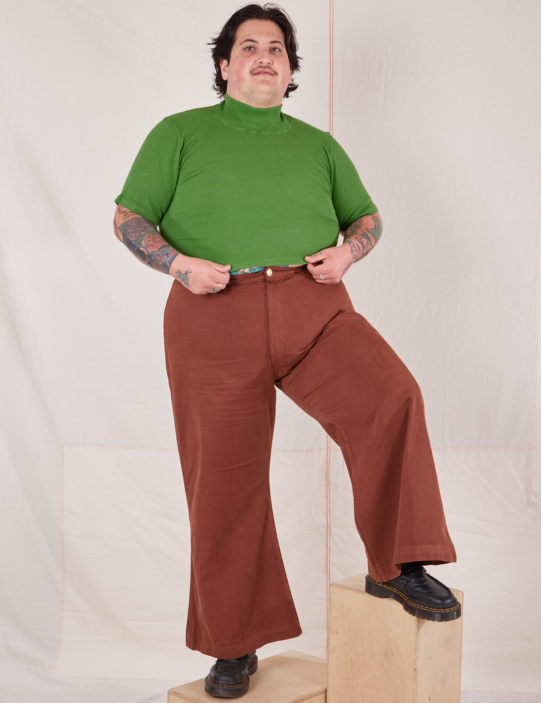 Sam is wearing size XL 1/2 Sleeve Essential Turtleneck in Bright Olive paired with fudgesicle brown Bell Bottoms