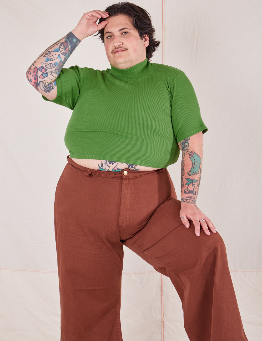 Sam is wearing 1/2 Sleeve Essential Turtleneck in Bright Olive and fudgesicle brown Bell Bottoms