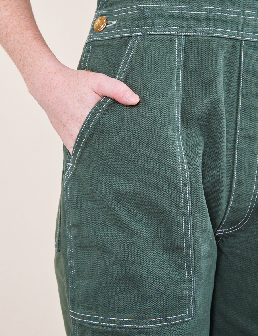 Front pocket close up of Original Overalls in Dark Emerald Green. Margaret has her hand in the pocket.