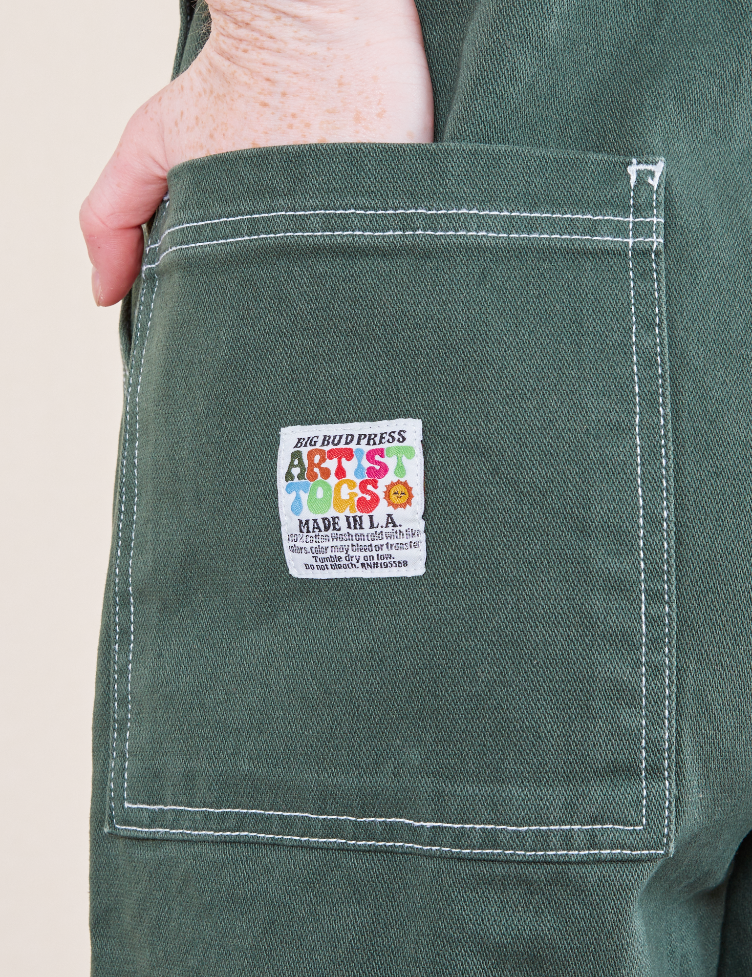 Back pocket close up of Original Overalls in Dark Emerald Green. Margaret has her hand in the pocket.