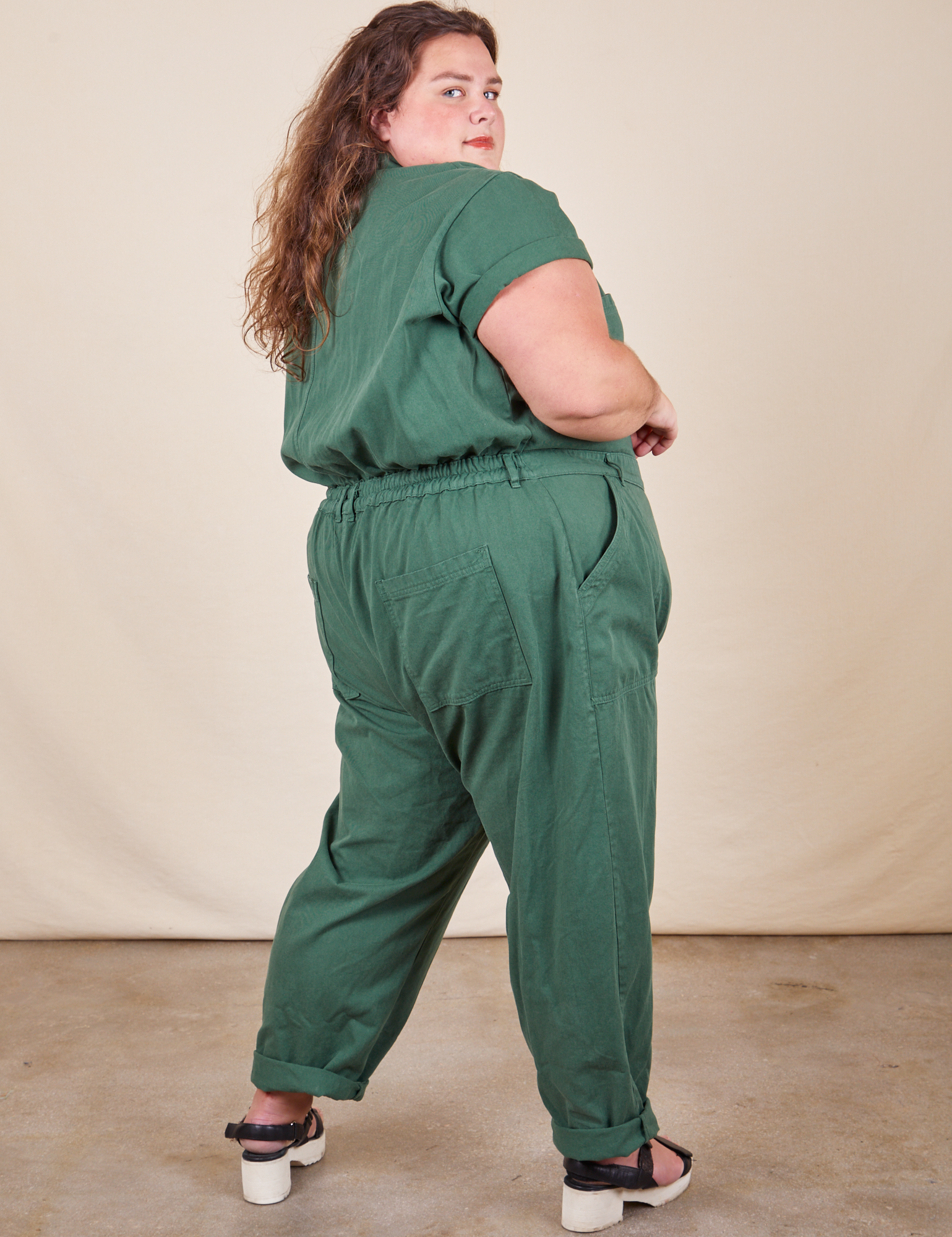 Angled back view of Short Sleeve Jumpsuit in Dark Emerald Green worn by Mara
