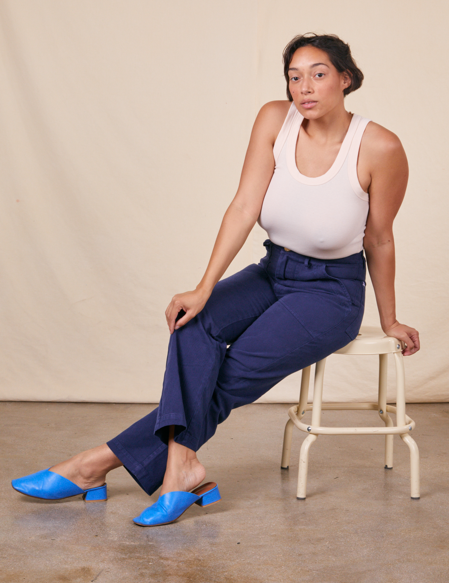 Tiara is sitting on a vintage stool wearing Work Pants in Navy Blue and vintage off-white Tank Top