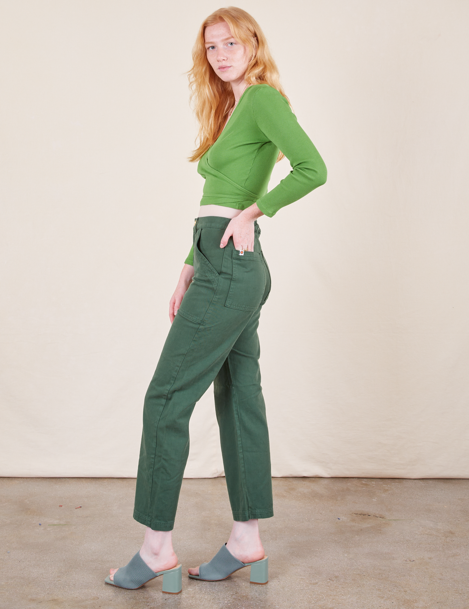 Side view of Work Pants in Dark Emerald Green and bright olive Wrap Top worn by Margaret
