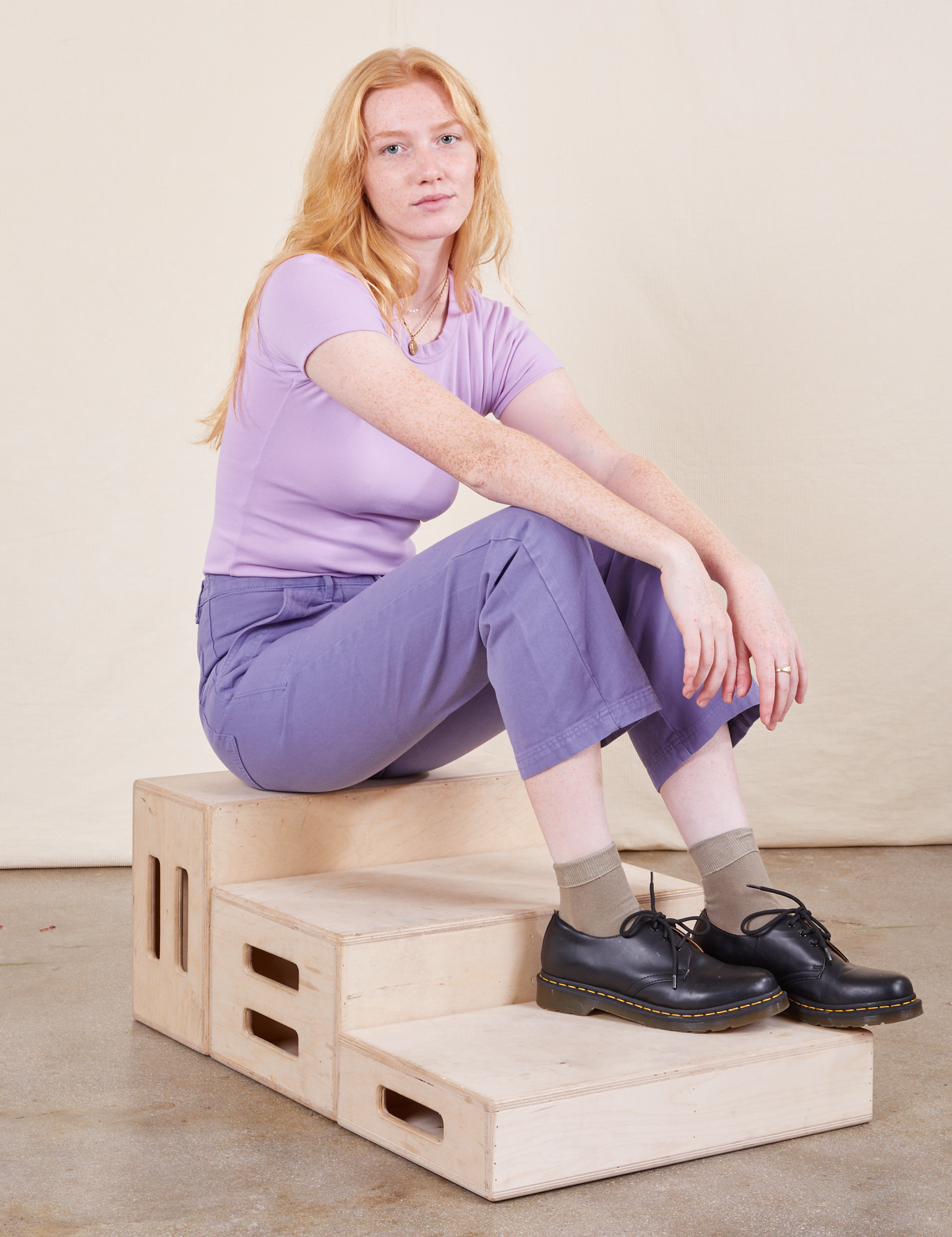 Margaret is sitting on a wooden crate wearing Work Pants in Faded Grape