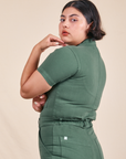 Angled side view of Short Sleeve Jumpsuit in Dark Emerald Green worn by Melanie
